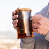 Person holding a Ukiyo glass mug with a wooden lid outdoors